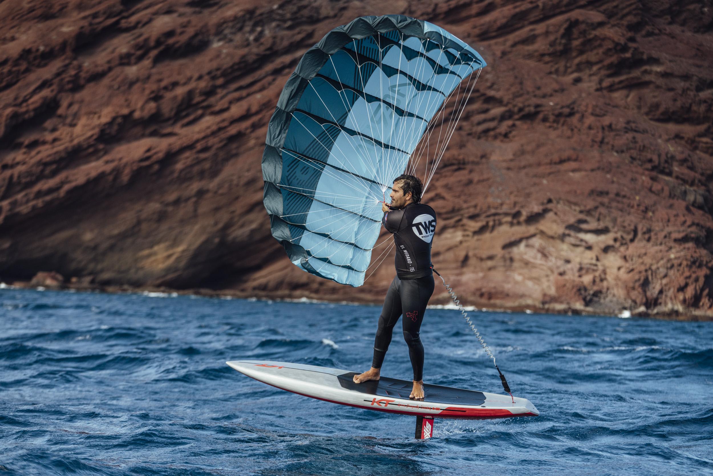 Parawing foiler riding past dramatic volcanic cliffs, showing the sport in a stunning coastal setting