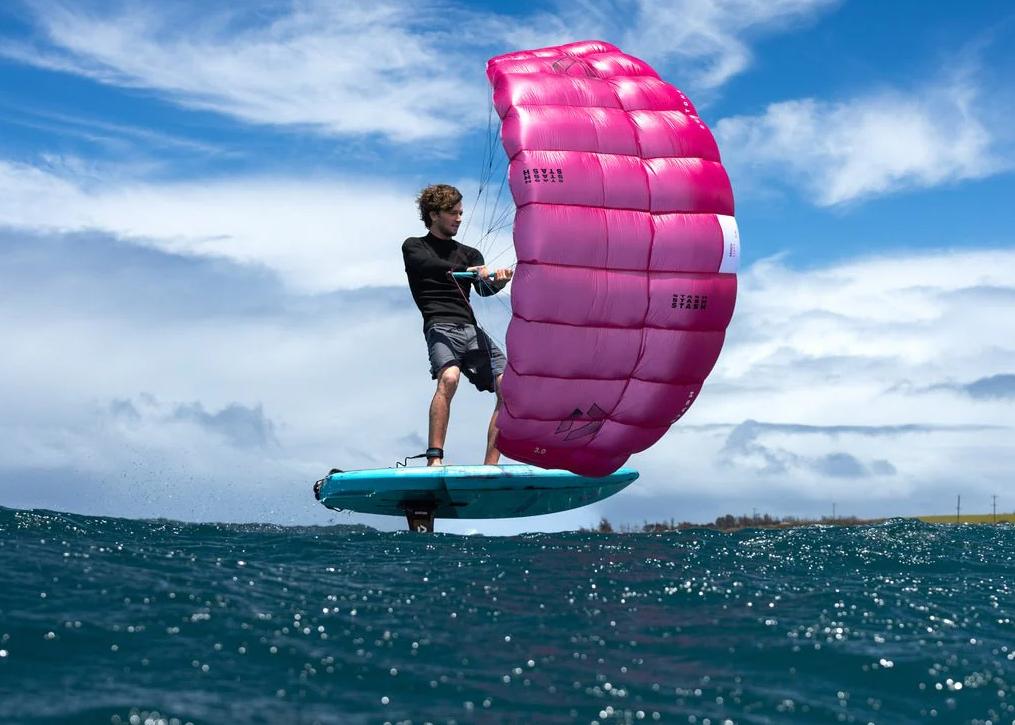 Rider foiling on the Duotone Stash parawing with vivid pink wing against blue sky