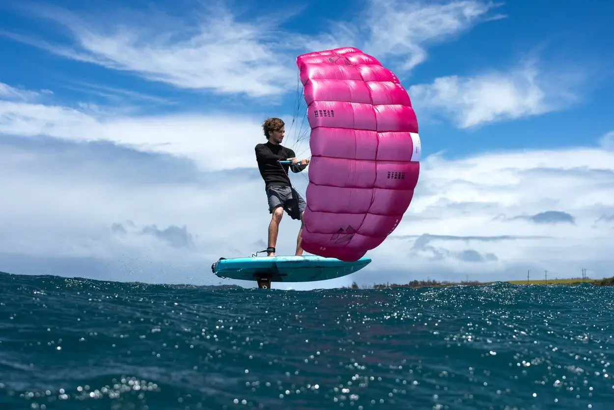 Duotone Stash rider foiling at low angle with pink wing fully inflated against blue sky