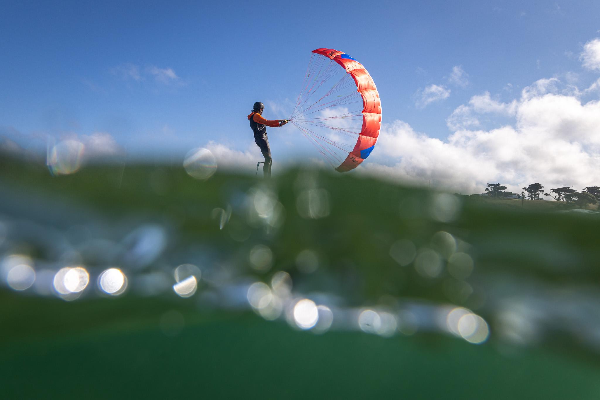 Flow D-Wing rider foiling with wing overhead, underwater bokeh in the foreground