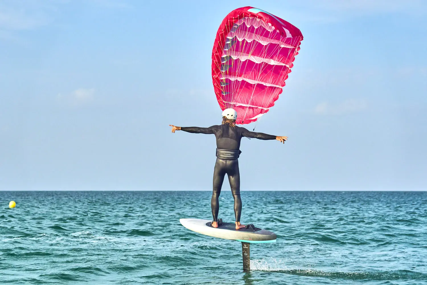Parawing foiler cruising with arms spread wide, demonstrating the hands-free harness-based riding experience