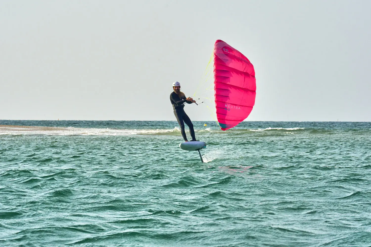 Gong Lowkite rider foiling with pink wing near a sandy coastal landscape