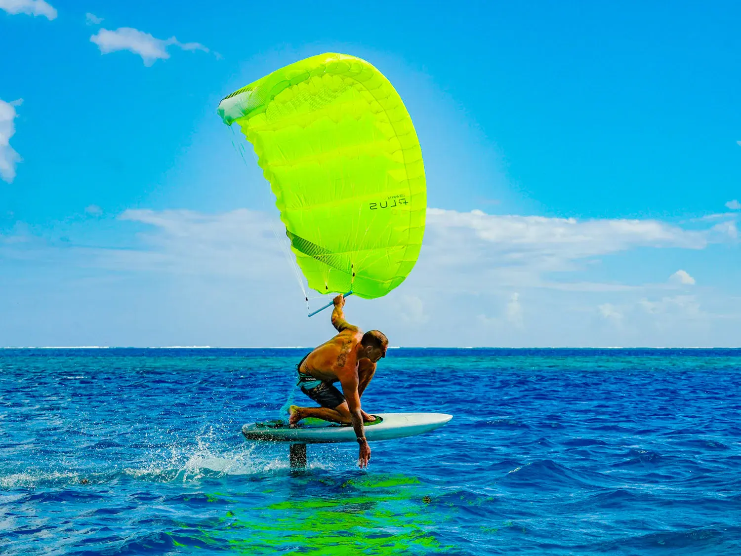 Gong Lowkite rider foiling in tropical blue water with vivid green wing fully deployed