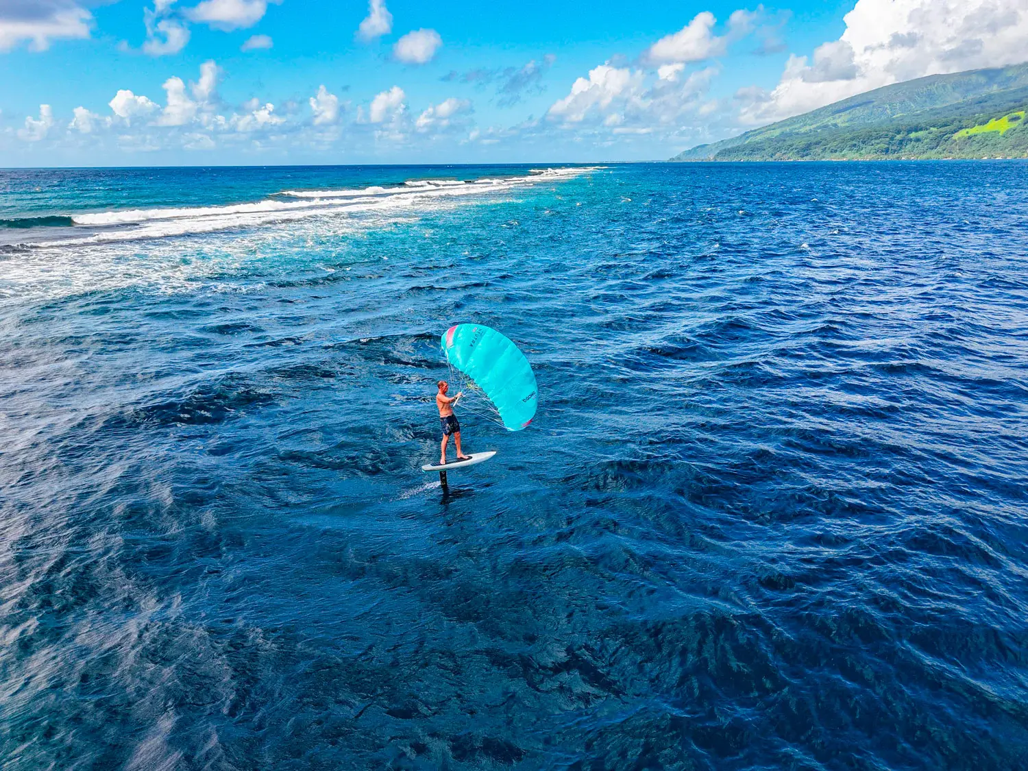 Drone view of parawing foiler riding across a wide ocean with mountains behind