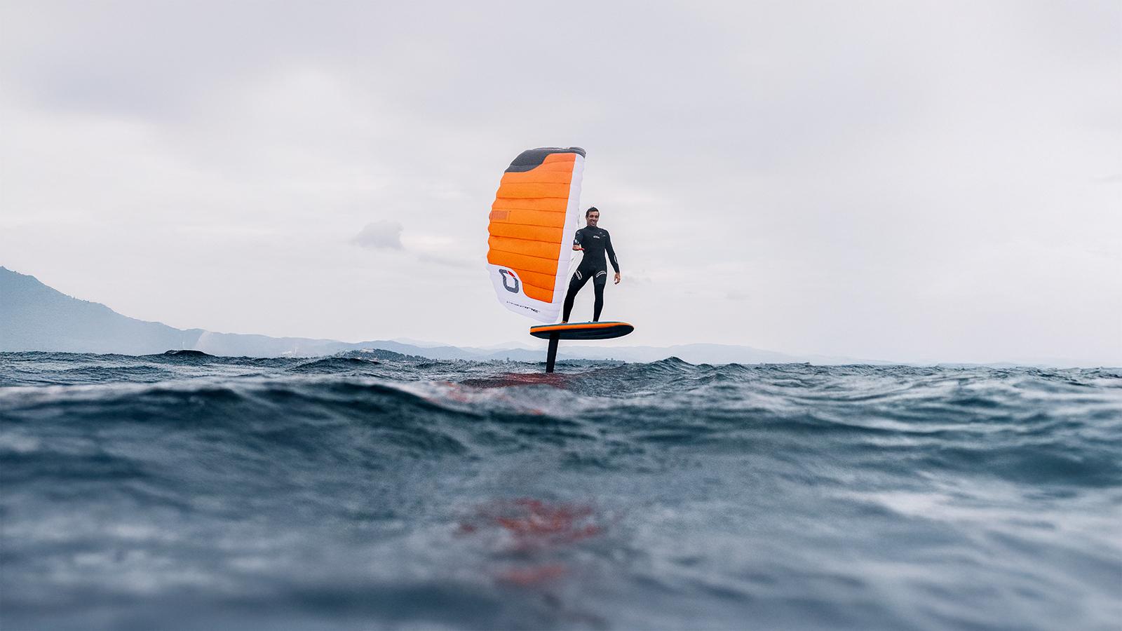 Ozone Pocket Rocket rider foiling with the parawing fully deployed, cinematic ocean backdrop