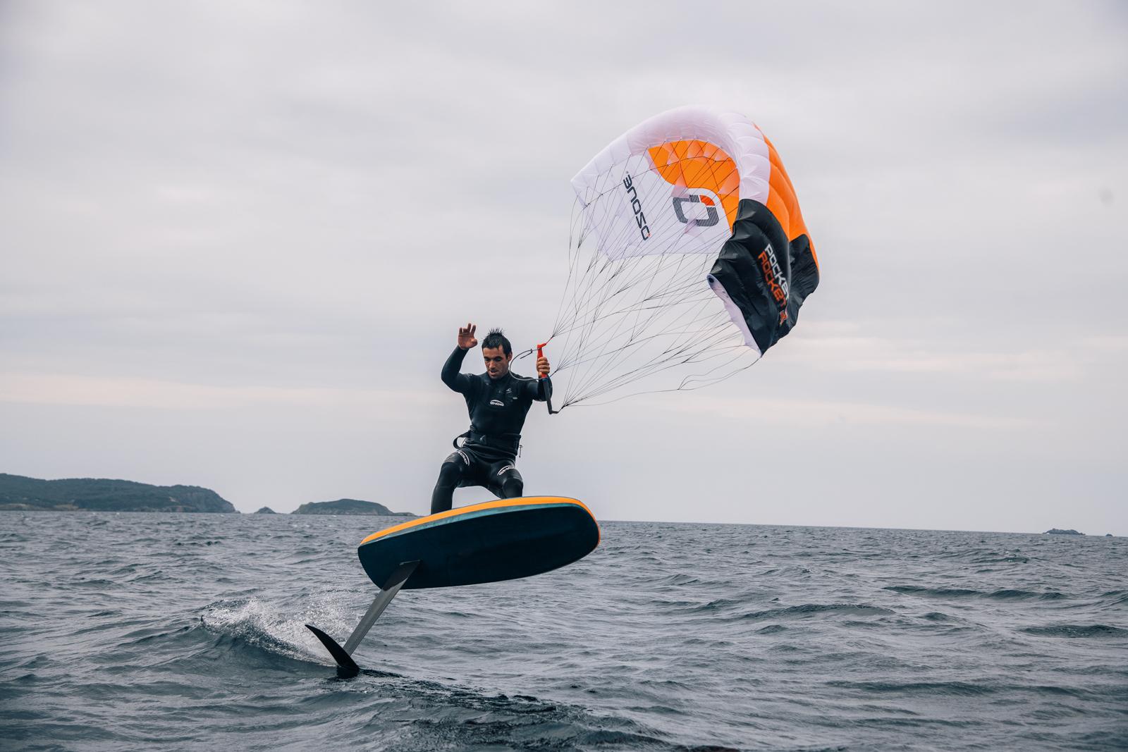Rider foiling with an Ozone Pocket Rocket parawing, waving at the camera from the water
