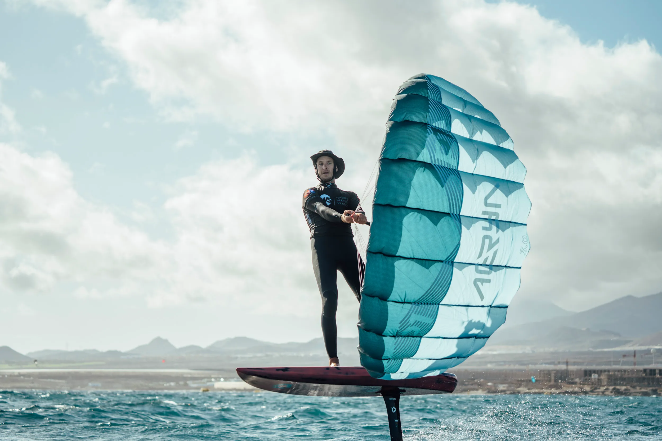 Aeryn P1 Pocket Wing rider foiling with wing branding visible against dramatic cloudy sky