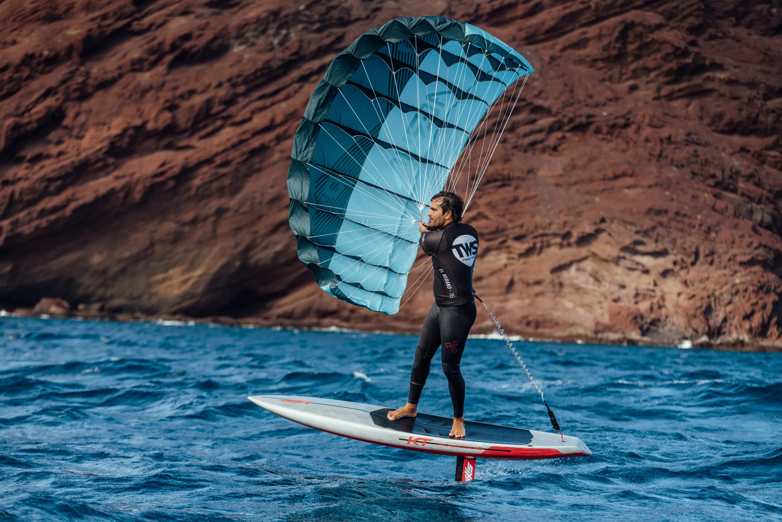 Parawingfoiler riding past dramatic volcanic cliffs, showing the sport in a stunning coastal setting