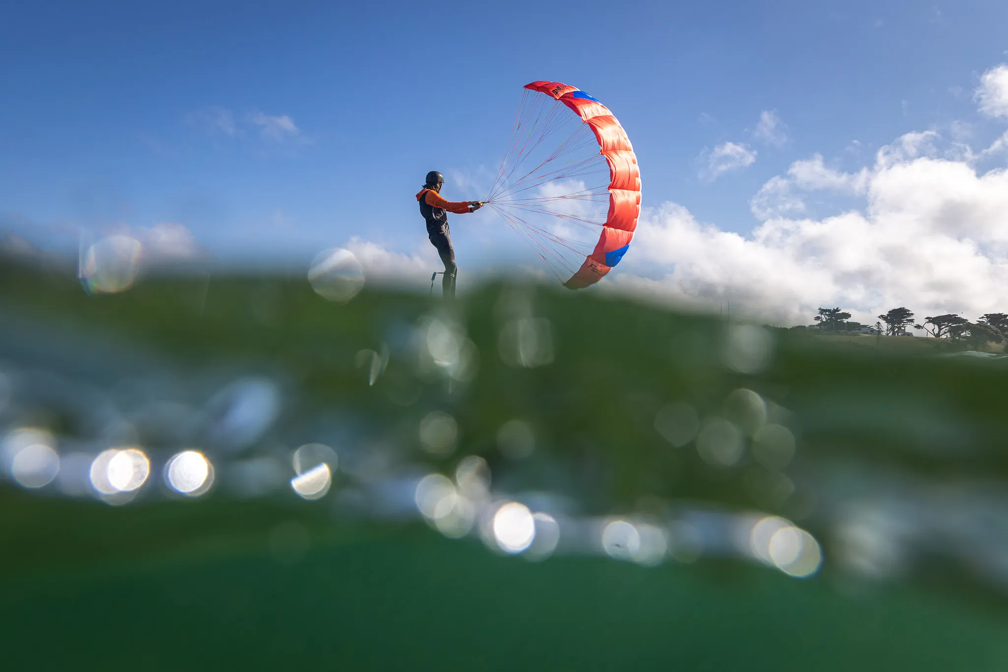 Flow D-Wing rider foiling with wing overhead, underwater bokeh in the foreground