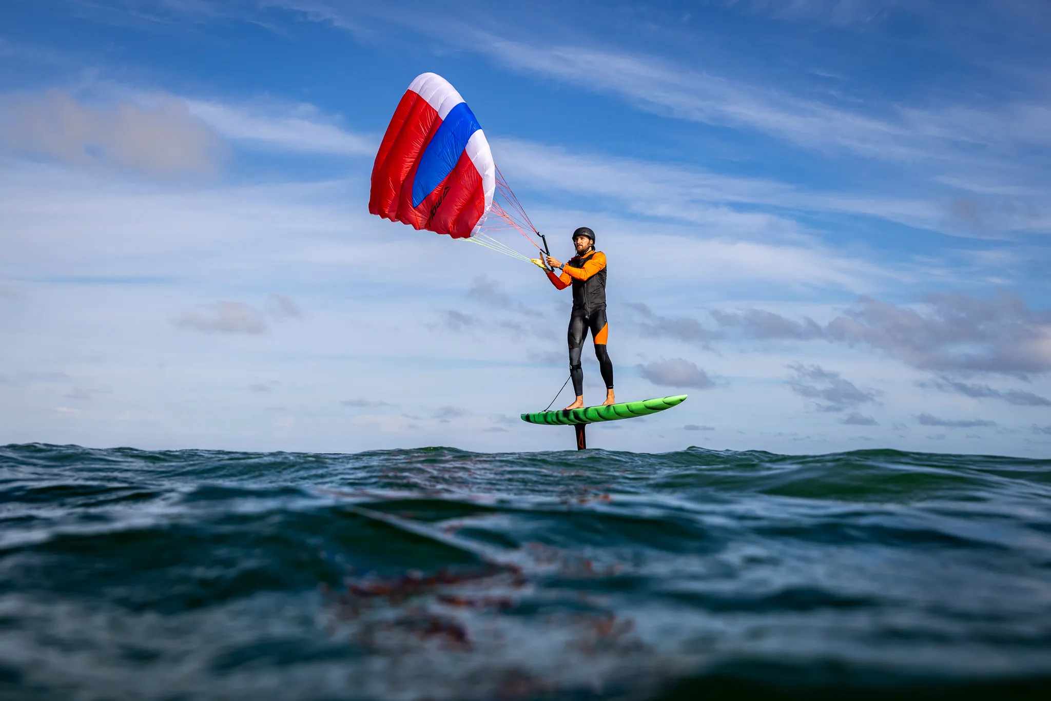 Flow D-Wing rider foiling with wing deployed against a wide ocean sky