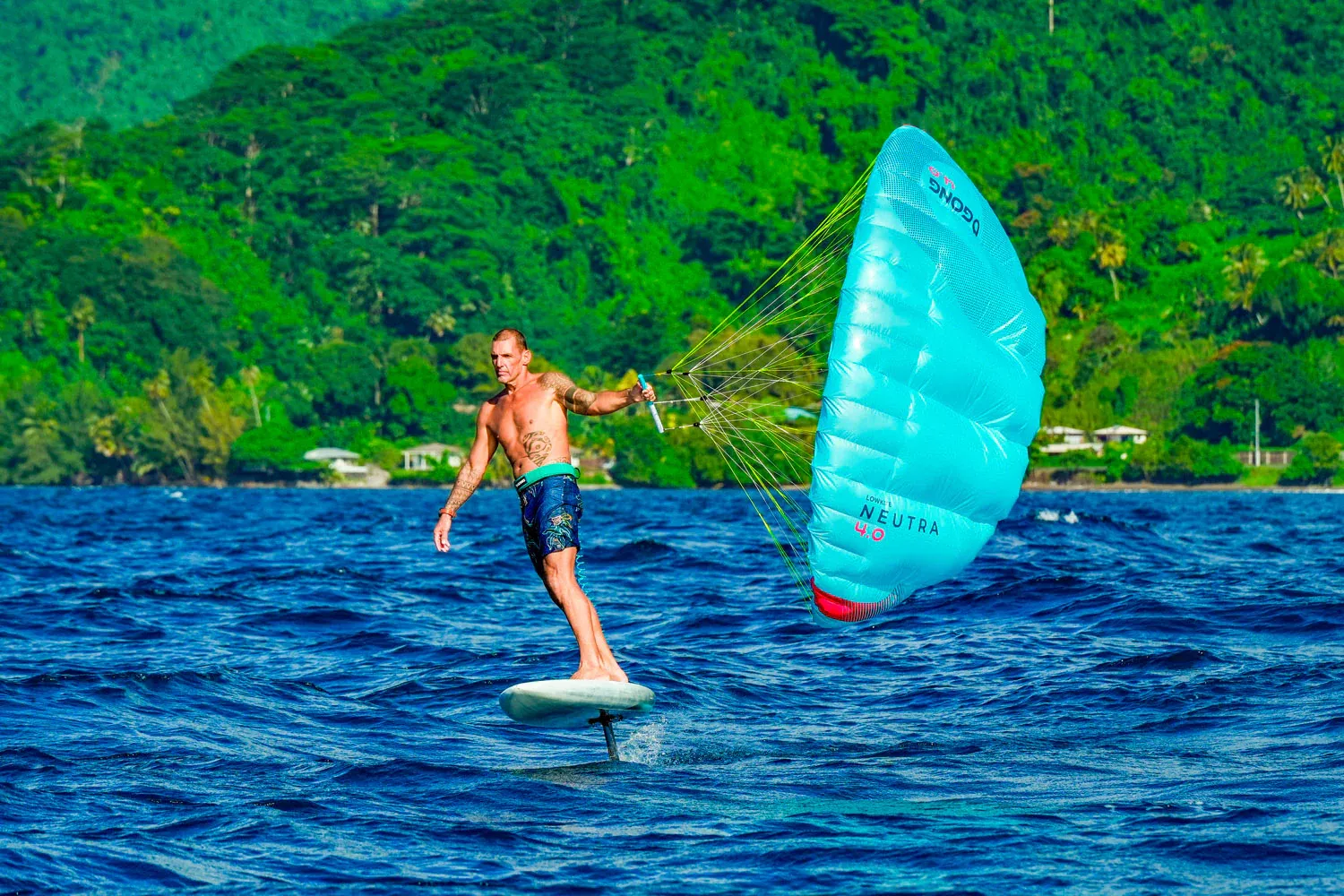 Parawingfoiler riding in tropical water with lush green mountains in the background