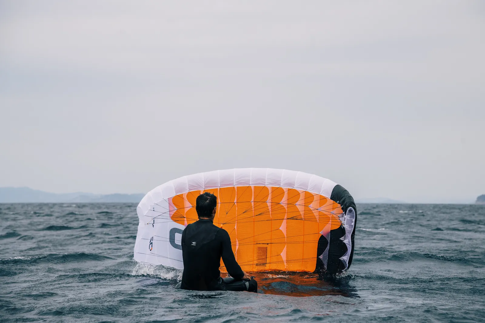 Ozone Pocket Rocket rider preparing for a water start, sitting with wing on the ocean surface